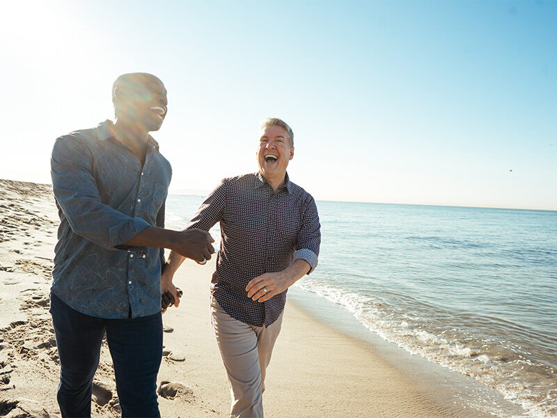 young male couple happy and laughing walking down the beach