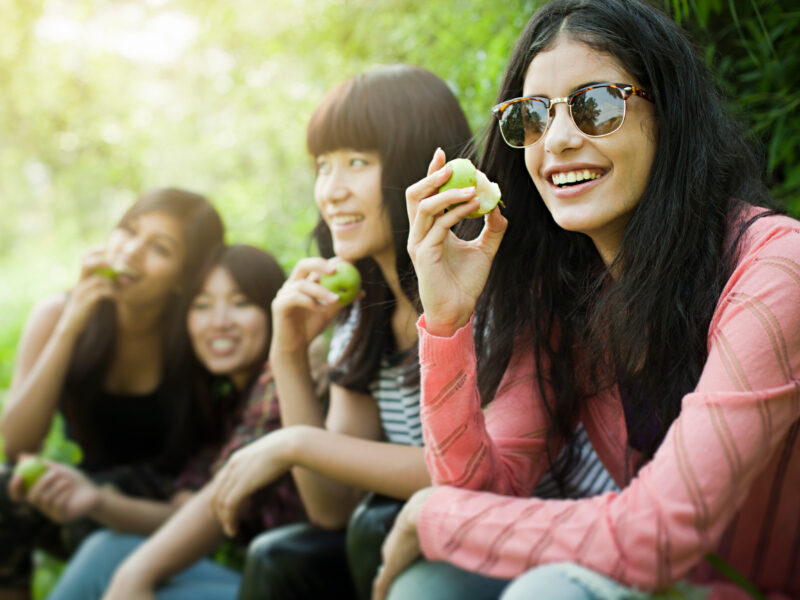 Girls smiling enjoying apples in a garden.